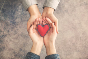 Man and woman hands guard a red cloth heart.