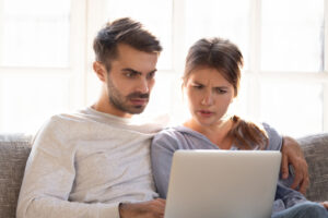 Confused baffled wife and shocked frustrated husband looking at computer. He is trying to break free from what breaks his marriage.