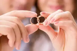 A man and woman smile and hold their wedding bands together as if they are interlocked, symbolizing prayers for marriage restoration.