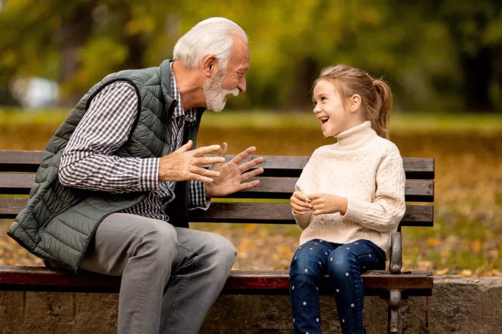 Grandparents and screen time — grandfather and granddaughter laughing together on a park bench, no devices.