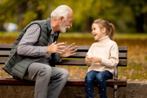 Grandparents and screen time — grandfather and granddaughter laughing together on a park bench, no devices.