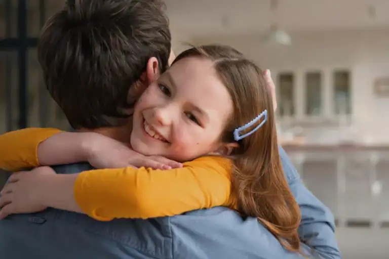 Laughing child hugs her daddy outdoors—a joyful moment of gratitude that helps raise grateful kids.