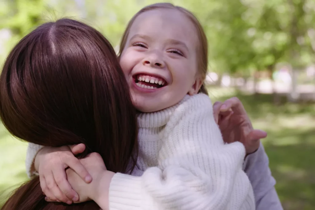 Laughing child hugs her mom outdoors—a joyful moment of gratitude that helps raise grateful kids.