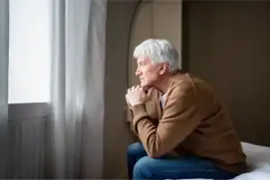 Older man sitting on the edge of a bed, reflecting quietly as he thinks about breaking generational curses.