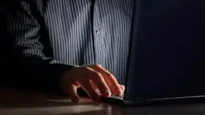 Close up of a man's hand typing on a laptop as he sits in the dark, symbolizing the impact of porn on a marriage