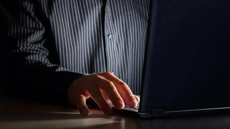 Close up of a man's hand typing on a laptop as he sits in the dark, symbolizing the impact of porn on a marriage