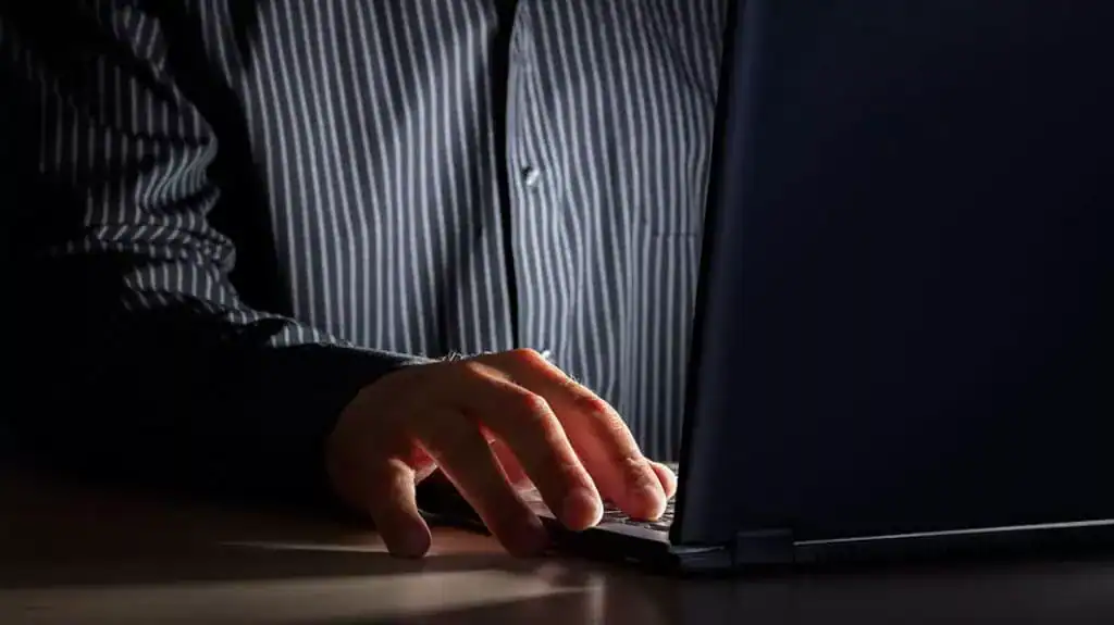 Close up of a man's hand typing on a laptop as he sits in the dark, symbolizing the impact of porn on a marriage