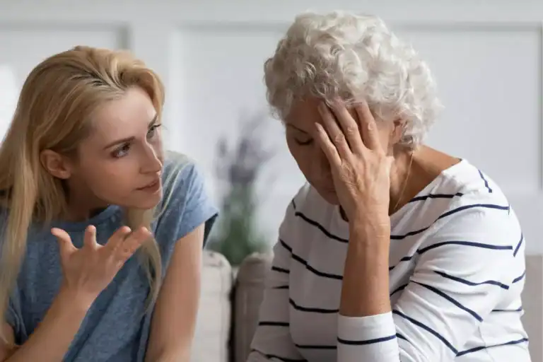 Mother and daughter sit on a couch, facing each other as one speaks with expressive hand gestures while the other listens with a hand resting near the face.