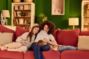 A person sitting on a red couch with two children resting closely on either side, illustrating a warm and structured family moment associated with authoritative parenting.