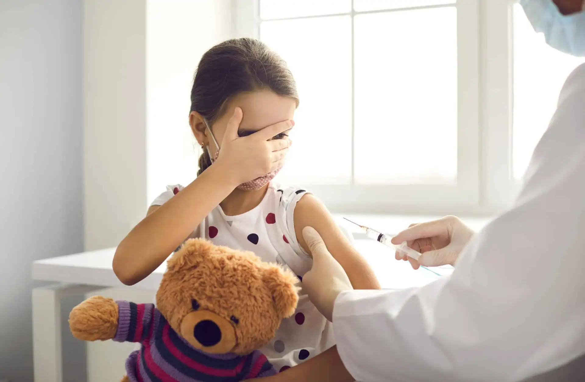 An anxious young girl about to receive a shot from a doctor