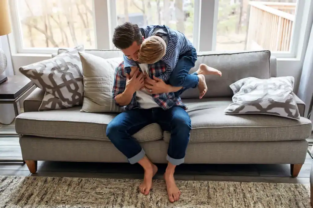 Father and son sharing a playful moment on a couch, illustrating biblical fatherhood through warmth, affection, and connection.