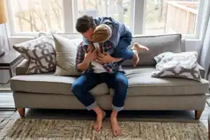 Father and son sharing a playful moment on a couch, illustrating biblical fatherhood through warmth, affection, and connection.