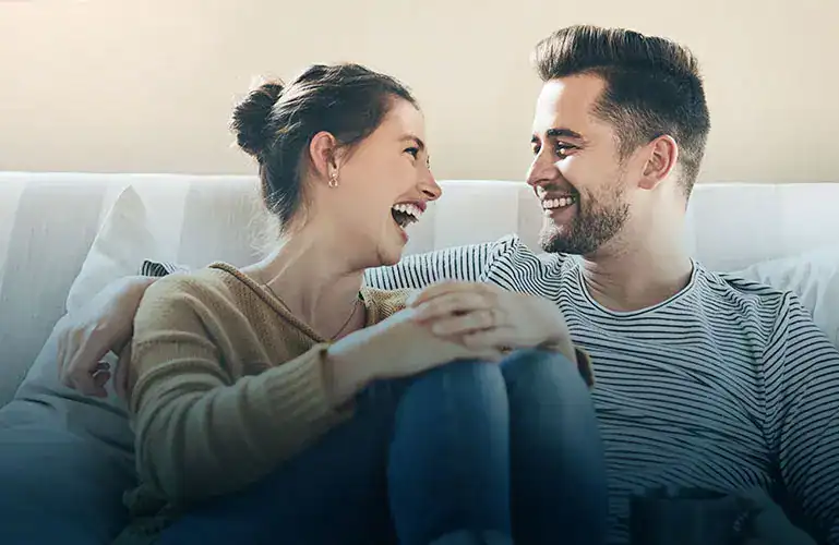 Smiling couple sitting close together on a couch, laughing and gazing at each other