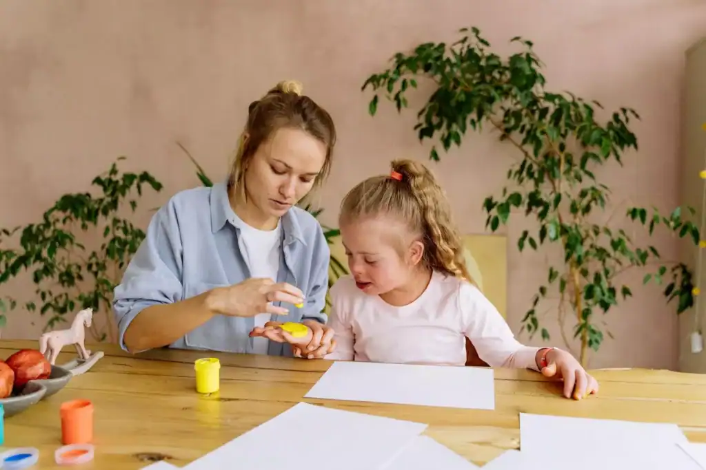 Mother helping her daughter with Down syndrome paint with fingers, supporting special needs development through hands-on play.