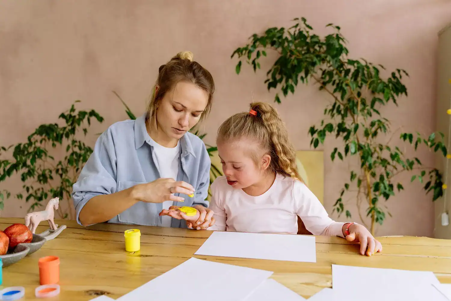 Mother helping her daughter with Down syndrome paint with fingers, supporting special needs development through hands-on play.