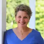 Headshot of Chris Seaton smiling warmly on a porch with a greenery blurred in the background.