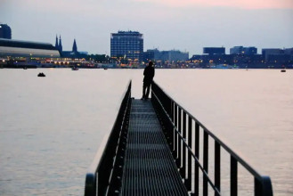 Man standing alone at the end of a pier looking at the cityscape in the distance