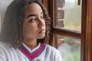 Teenage girl gazing pensively out a window, reflecting the isolation and hidden pain often explored in questions about why teens commit suicide.