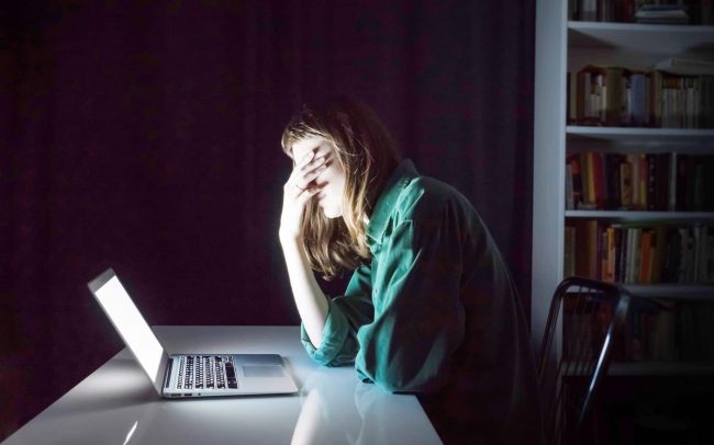 Regretful woman sitting in front of her laptop in a dark room Regretful woman sitting in front of her laptop in a dark room